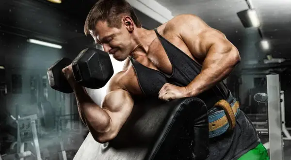 Kulturysta z determinacją ćwiczy biceps, napinając mięsień trójgłowy ramienia podczas podnoszenia ciężaru.