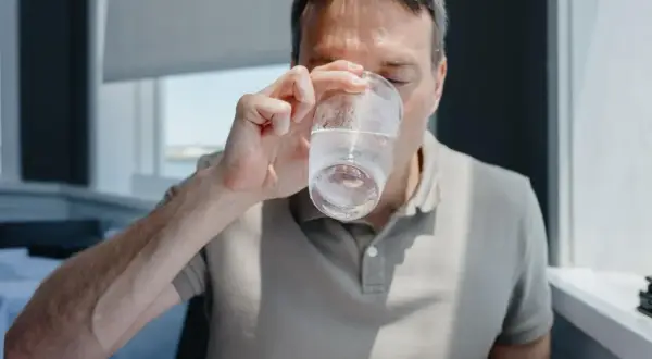 Mężczyzna pije wodę, zastanawiając się, ile pić wody, żeby schudnąć. Woda jest kluczem do zdrowia i metabolizmu.