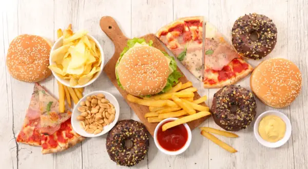 Uczta z niezdrowym jedzeniem: burgery, frytki, pizza, pączki, chipsy i orzeszki.