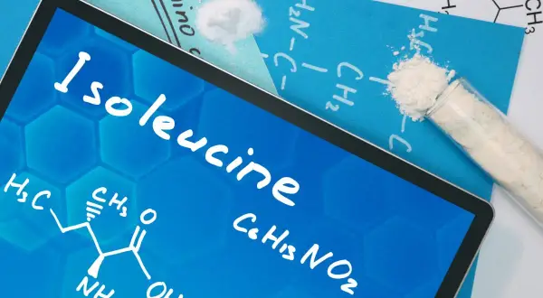 Na ekranie tabletu widnieje nazwa "Isoleucine" oraz wzór chemiczny. Obok leżą próbki białego proszku, przypominające izoleucynę.
