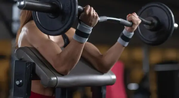 Kobieta ćwiczy biceps na modlitewniku, podnosząc sztangę. Zastanawiasz się, ile waży gryf?