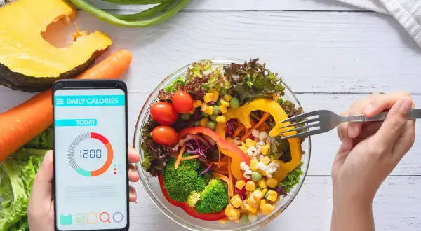 Zdrowa sałatka i smartfon z aplikacją "Daily Calories" pokazującą 1200 kcal. To najlepsza aplikacja do liczenia kalorii, która pomoże Ci osiągnąć cel.