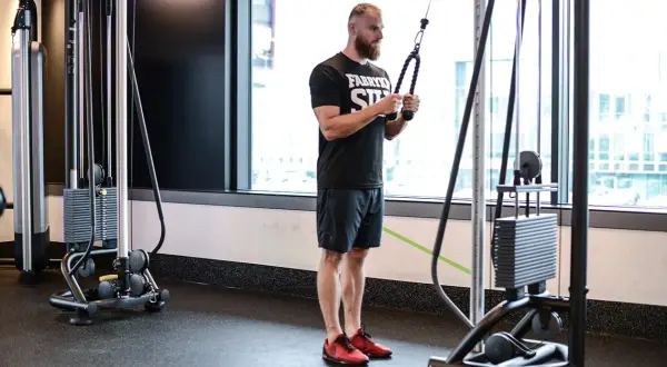 Mężczyzna wykonuje ćwiczenie na triceps, znane jako skull crushers, używając wyciągu.