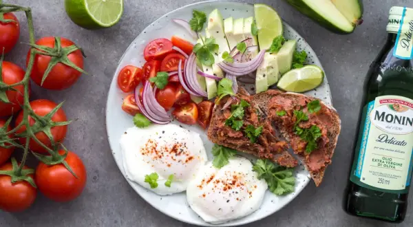Śniadanie idealne na dietę 1500 kcal: jajka w koszulce, tost z pastą, awokado, pomidorki, cebula i limonka.