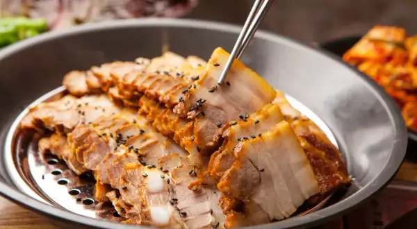 Plasterki gotowanego boczku, posypane czarnym sezamem, idealne na dietę mięsną. Obok widać kimchi.