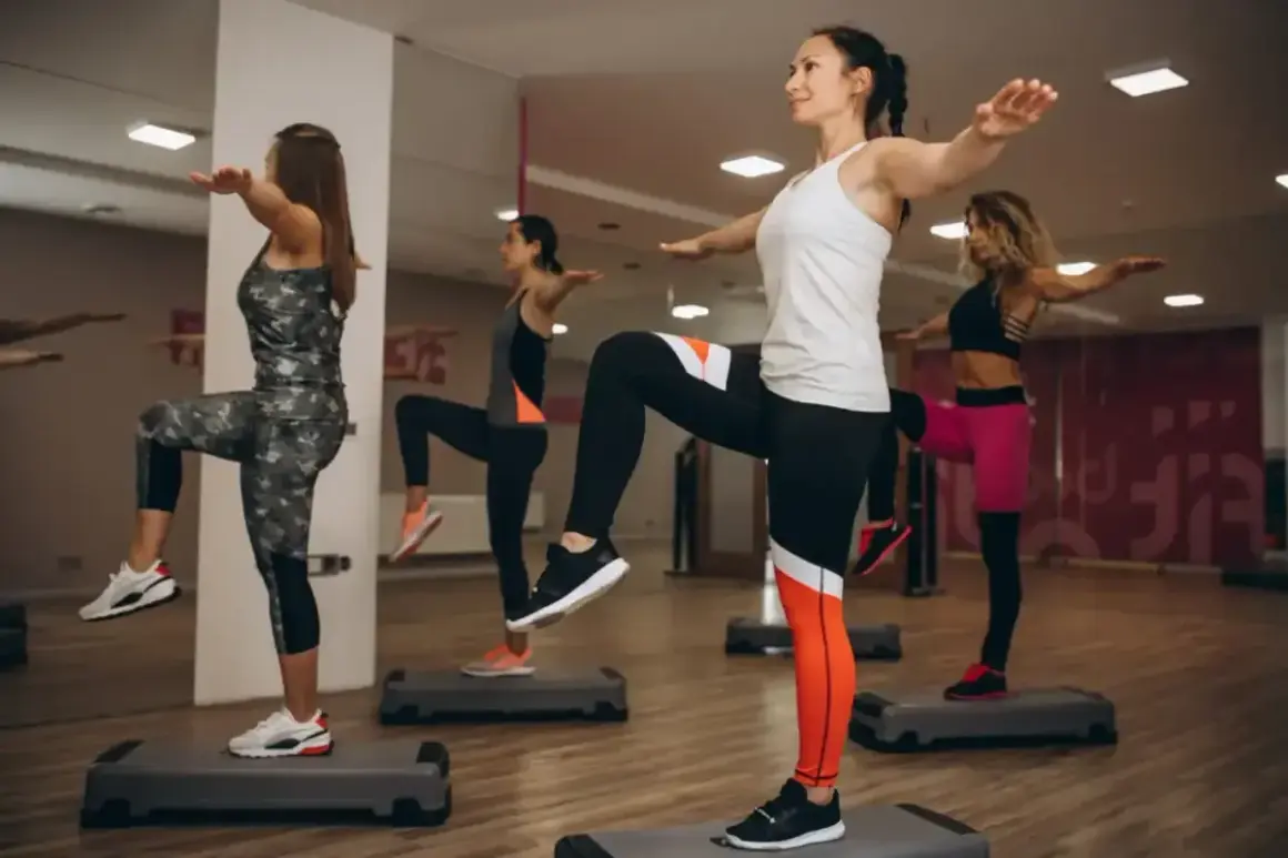 Kobiety wykonują trening aerobowy na stepach, podnosząc kolana i wyciągając ręce.