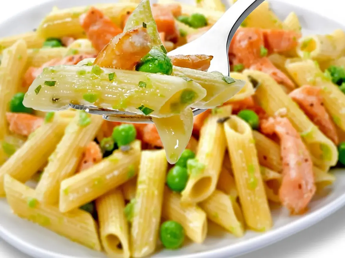 Penne z łososiem i groszkiem, polane kremowym sosem. Widok z bliska na widelcu.