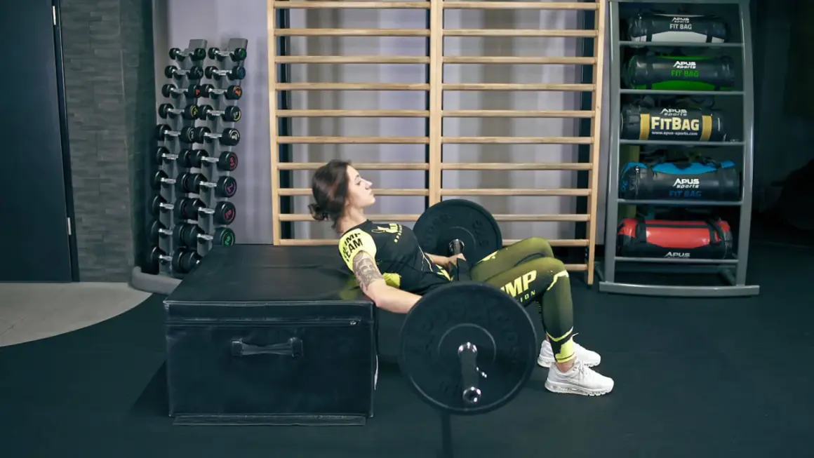 Kobieta wykonuje ćwiczenie hip thrusts z obciążeniem na ławce w siłowni.