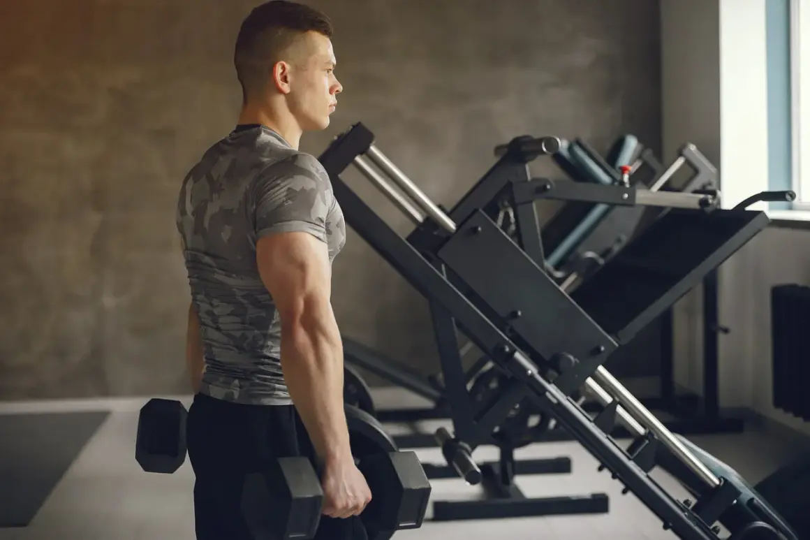 Mężczyzna z hantlami, ćwiczący triceps w siłowni.