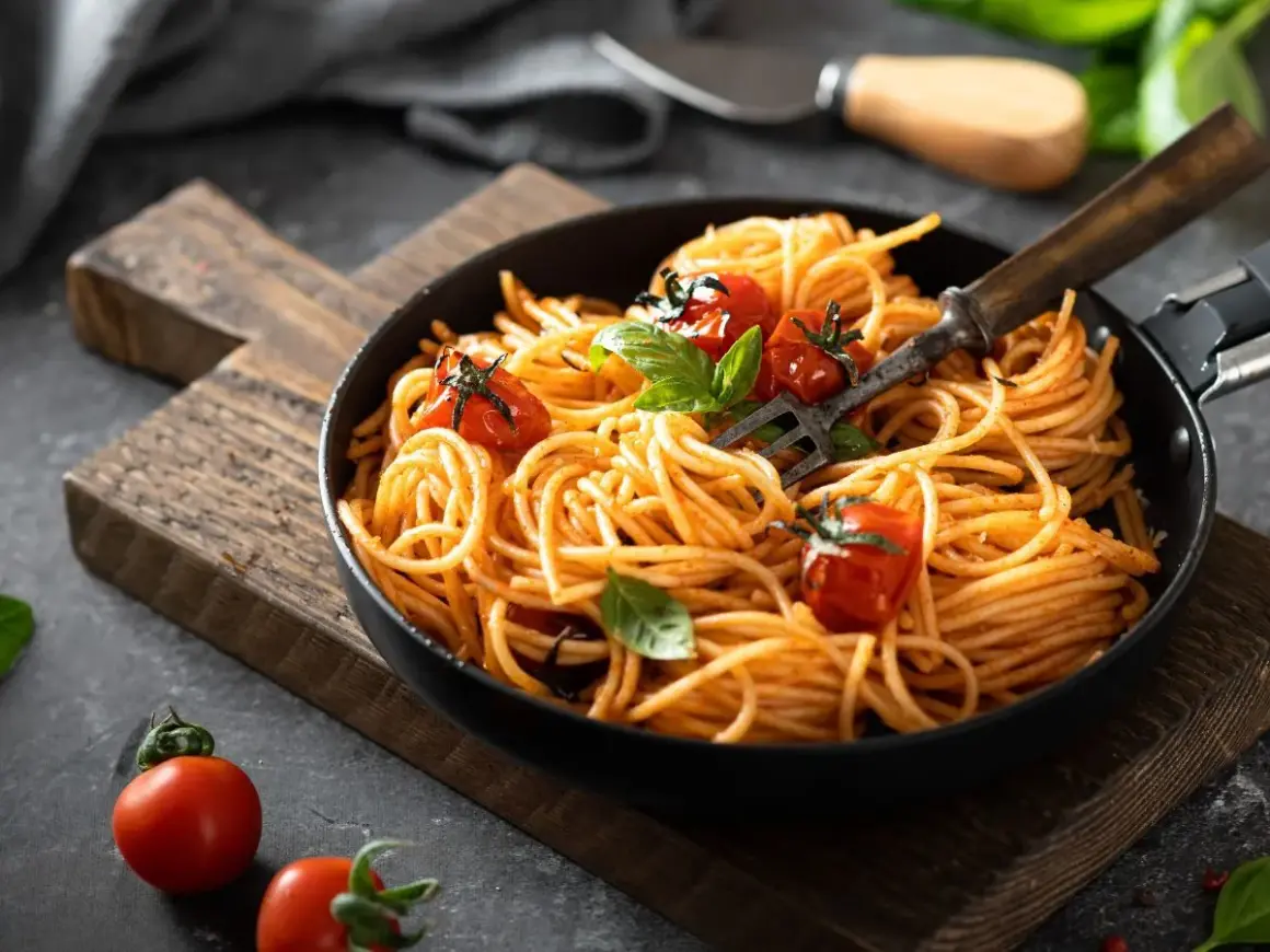 Pyszne danie z makaronem spaghetti w sosie pomidorowym, udekorowane świeżymi pomidorkami i bazylią. Idealne na szybki obiad.