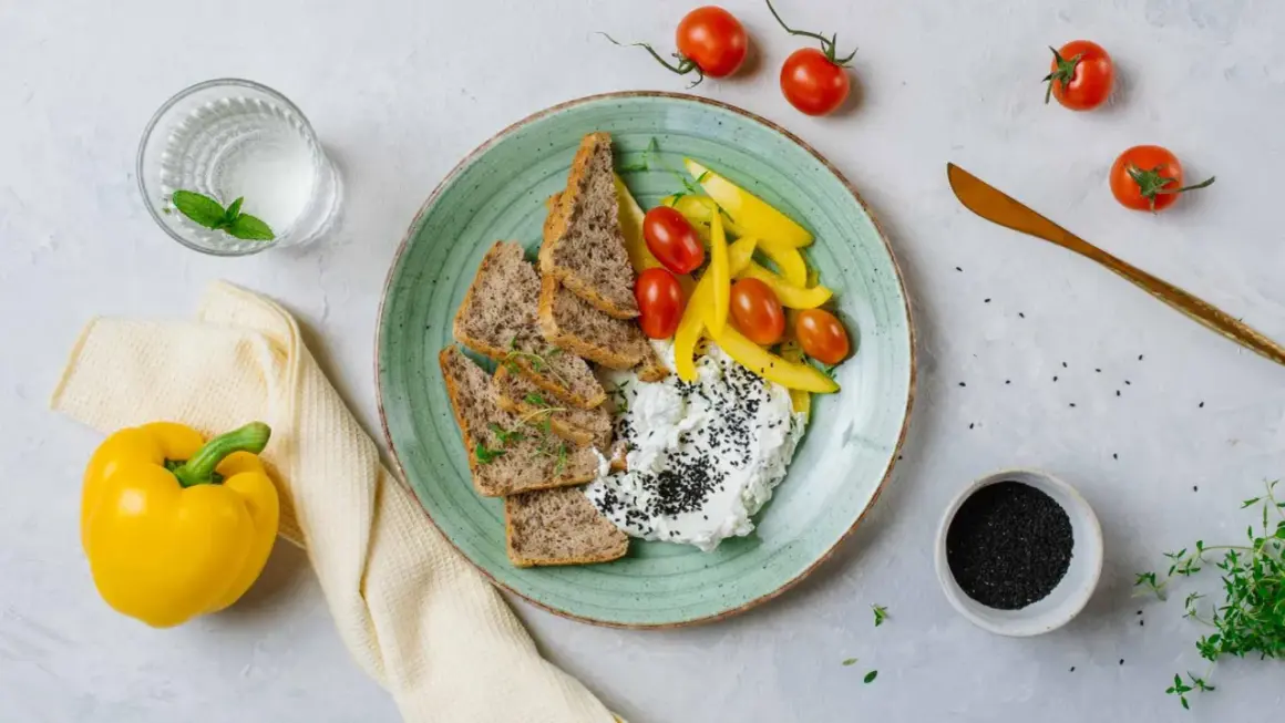 Szybkie posiłki wysokobiałkowe: twarożek z czarnuszką, pieczywo, pomidorki i papryka. Idealne na lekki lunch.