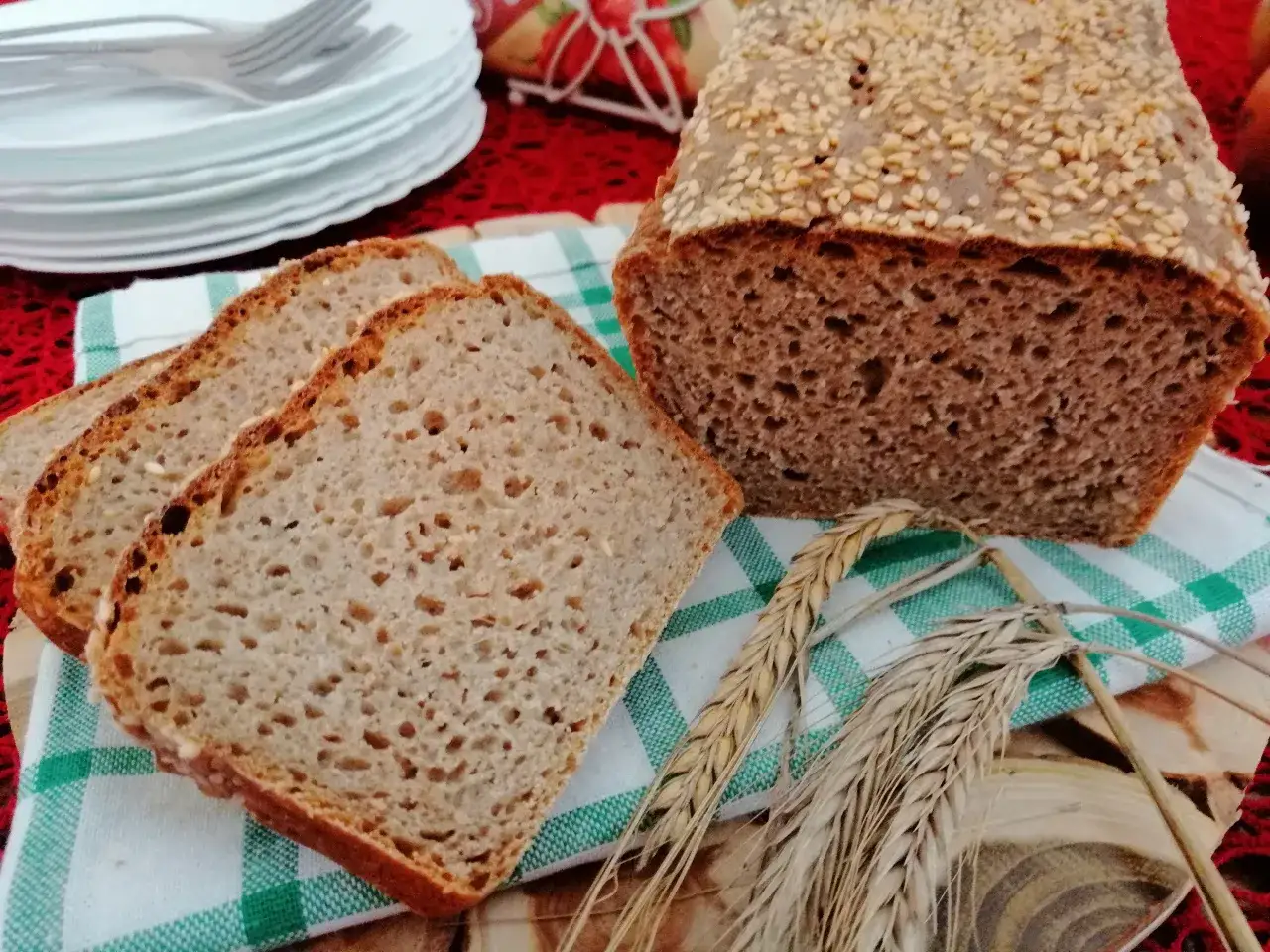 Chleb pełnoziarnisty z sezamem, idealny jako jaki chleb na odchudzanie. Kromki na zielono-białej serwetce, obok kłosy zbóż.