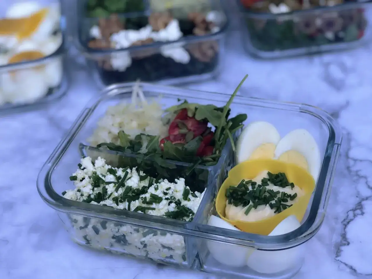 Gotowe keto śniadanie do pracy: jajka, twarożek z szczypiorkiem, rukola z pomidorkami i pestkami, surówka.