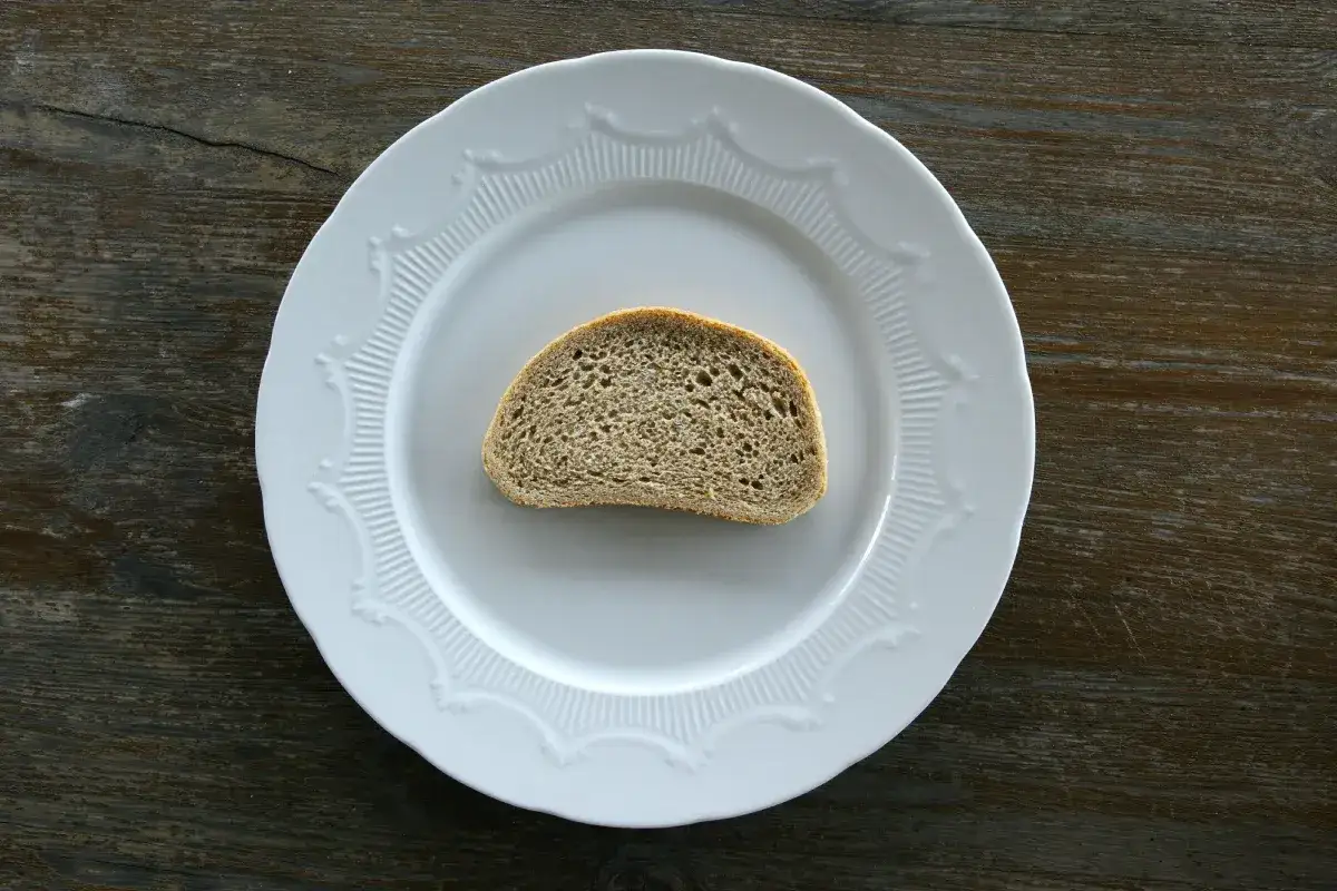 Jeden plasterek chleba pszennego na białym talerzu. Zastanawiasz się nad jego kcal?