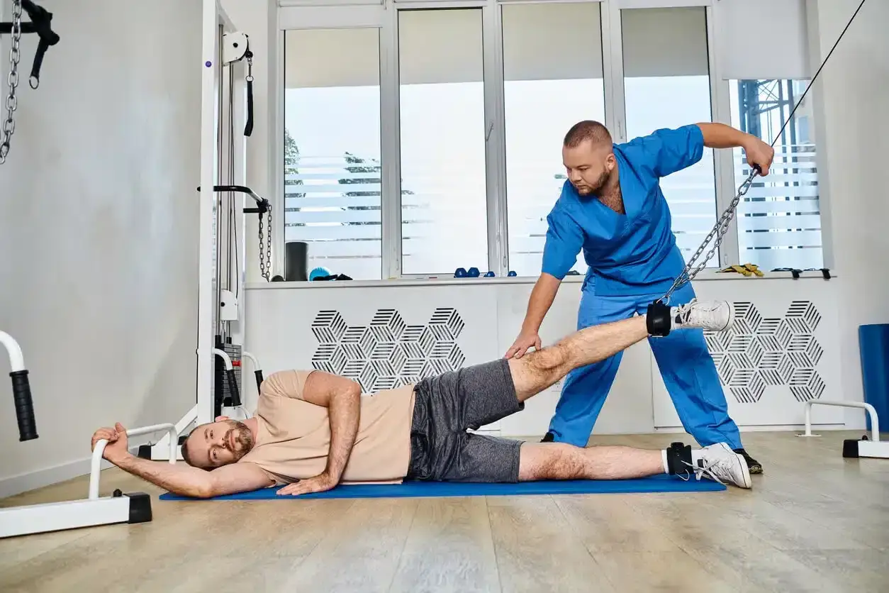 Rehabilitacja po zerwaniu mięśnia. Fizjoterapeuta pomaga pacjentowi w ćwiczeniach z użyciem wyciągu.