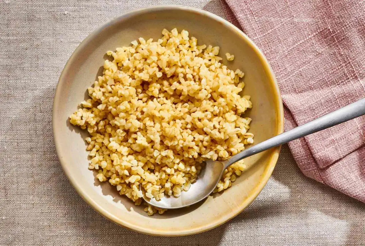 Miseczka pełna kaszy bulgur, która ma niski indeks glikemiczny. Obok leży łyżka i różowa serwetka.