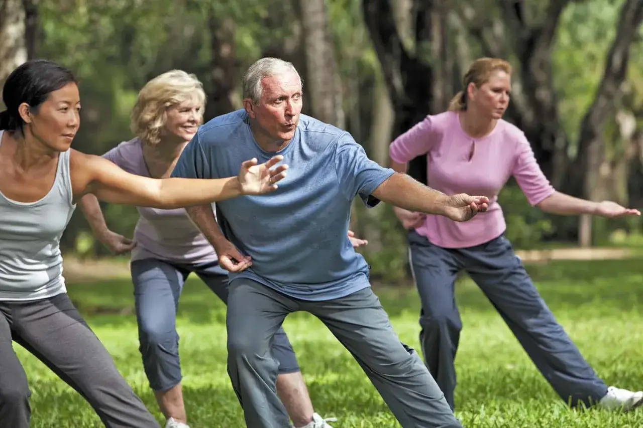 Grupa osób ćwiczy tai chi na trawie. Zastanawiasz się tai chi co to? To łagodna sztuka walki i forma medytacji w ruchu.