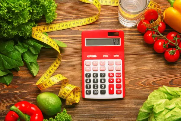 Czerwony kalkulator obok miarki i świeżych warzyw. Zastanawiasz się, ile to kcal? Oblicz swoją dietę!