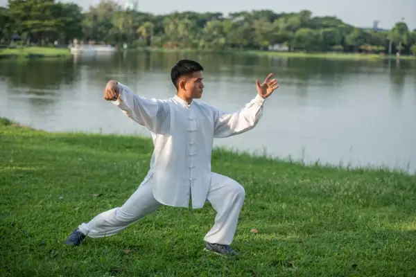 Mężczyzna w białym stroju ćwiczy tai chi co to za sztuka walki, harmonijnie poruszając się nad jeziorem.