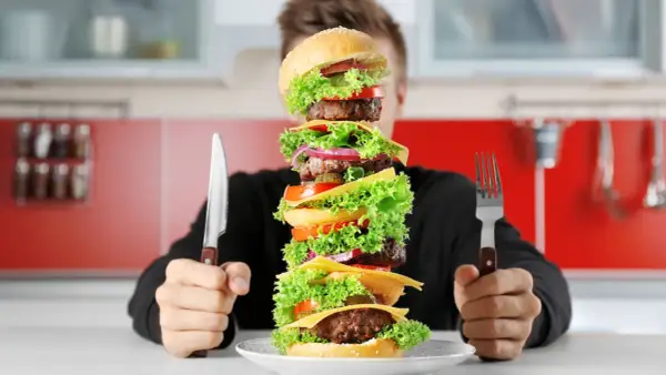 Człowiek z nożem i widelcem przed gigantycznym, wielopoziomowym burgerem. Czy to wyzwanie na omad?