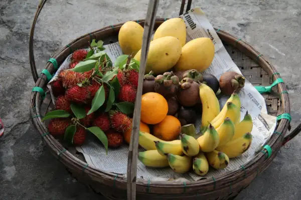 Koszyk pełen owoców: liczi, mango, pomarańcze, mangostany i banany. To idealne, lekkostrawne owoce na zdrową przekąskę.