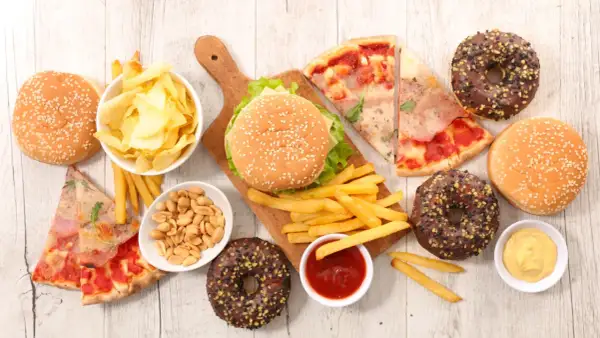 Uczta z niezdrowym jedzeniem: burgery, frytki, pizza, pączki, chipsy i orzeszki.