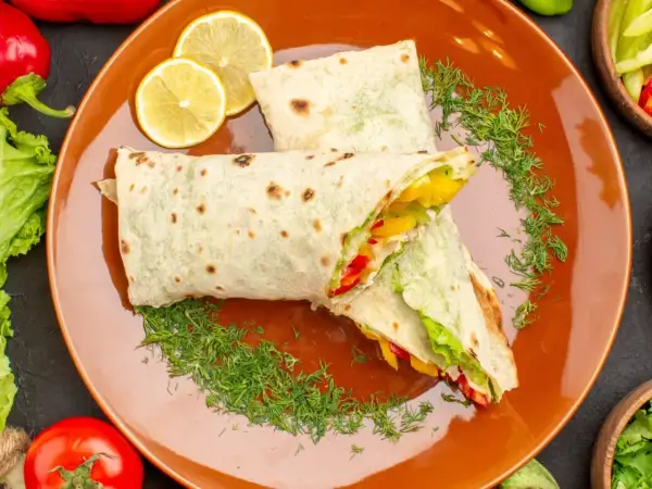 Dwa pyszne wrapy z warzywami i kurczakiem, podane na pomarańczowym talerzu z plasterkami cytryny i koperkiem. Idealny fit tortilla na szybki posiłek.