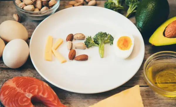 Czy dieta keto jest zdrowa? Na talerzu litery KETO z sera, orzechów, brokuła i jajka. Wokół łosoś, awokado, oliwa.