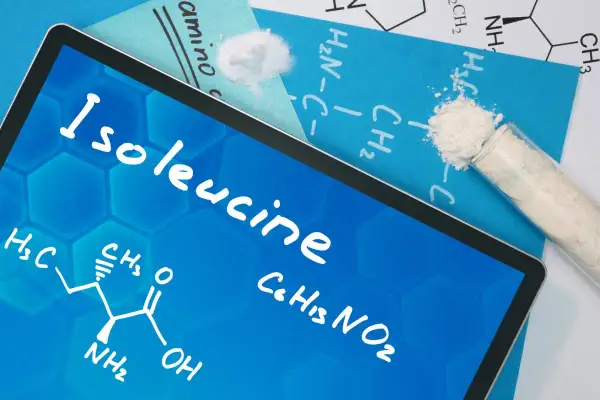 Na ekranie tabletu widnieje nazwa "Isoleucine" oraz wzór chemiczny. Obok leżą próbki białego proszku, przypominające izoleucynę.