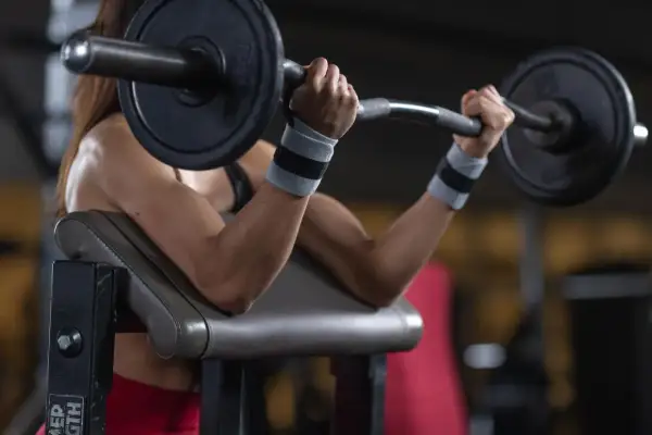 Kobieta ćwiczy biceps na modlitewniku, podnosząc sztangę. Zastanawiasz się, ile waży gryf?