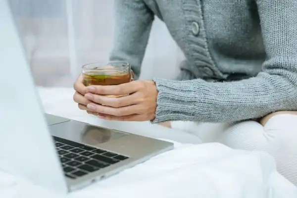 Kobieta w szarym swetrze pije herbatę, zastanawiając się, l teanina co to. Obok leży laptop.