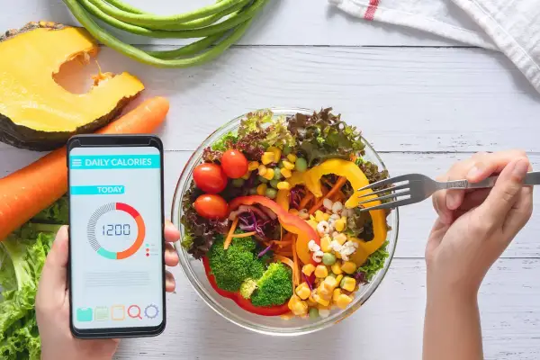 Zdrowa sałatka i smartfon z aplikacją "Daily Calories" pokazującą 1200 kcal. To najlepsza aplikacja do liczenia kalorii, która pomoże Ci osiągnąć cel.