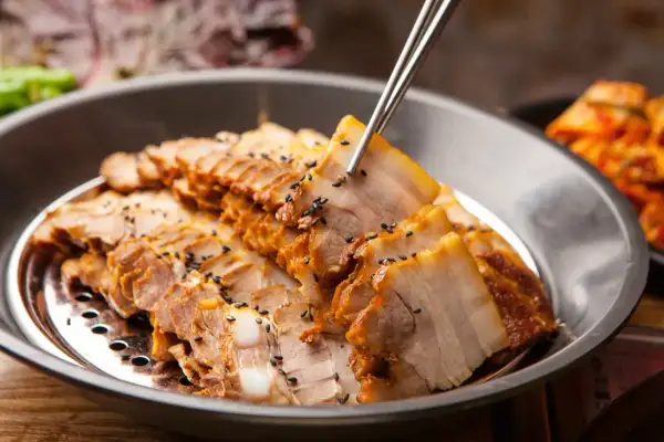 Plasterki gotowanego boczku, posypane czarnym sezamem, idealne na dietę mięsną. Obok widać kimchi.